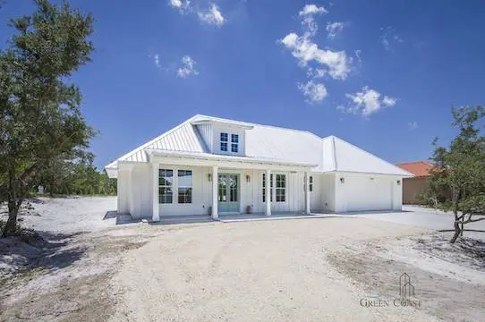 Coastal-Cottage-Island-House-Efficient-Hurricane-Safe Exterior quarter view of the front fascia of a small white cottage. Custom built by Green Coast Living. Surrounded by native flora and white sand, this simple and elegant home is designed to resist the elements. Built to Gold Fortified standards, it can withstand hurricanes and heat waves with ease.