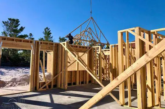 House-Framing-Custom-Home-Building-Gulf-Shores A matrix of fresh lumber framing stands proud in the morning sun as a crane hoists the first roof truss into place.