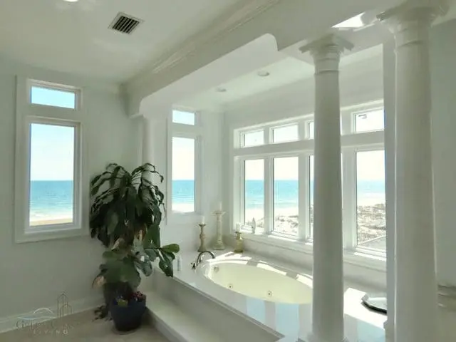 Custom Remodeled Bathroom with a beach view. Marble Soaking bathtub surrounded by windows, plants, and pillars. Renovation in Gulf Shores, AL.