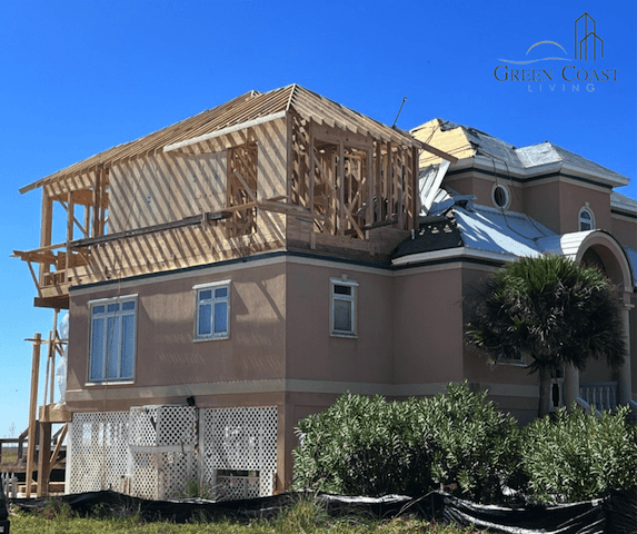 An exterior view of a beach house undergoing a third story addition. Framing is exposed and the sky is blue.