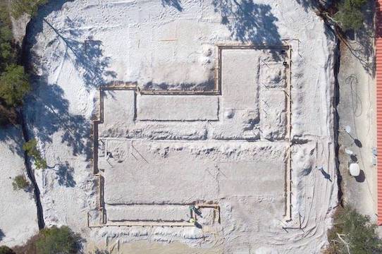 An aerial view of the foundation work being done for a family house. Precise trenches score the white beach sand like  the were drawn by a skilled architect.