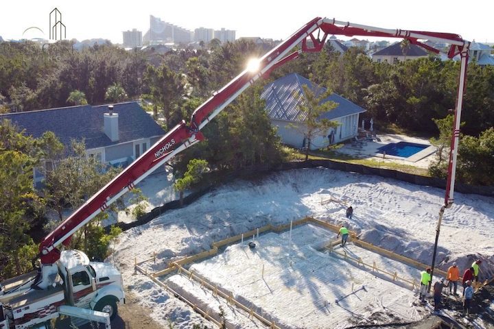 A large crane stretches over the future site of a house. The early morning sun reflects off the arm as it pumps concrete.