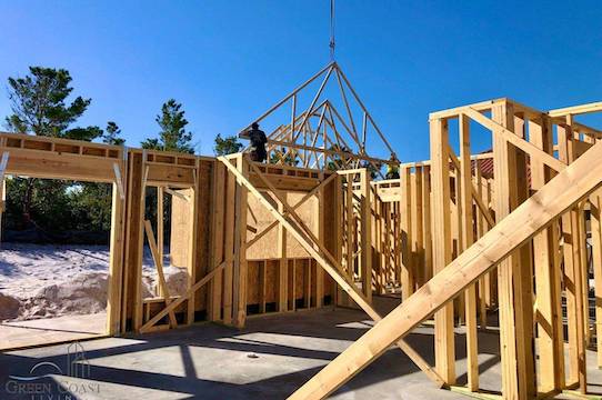 A matrix of fresh lumber framing stands proud in the morning sun as a crane hoists the first roof truss into place.