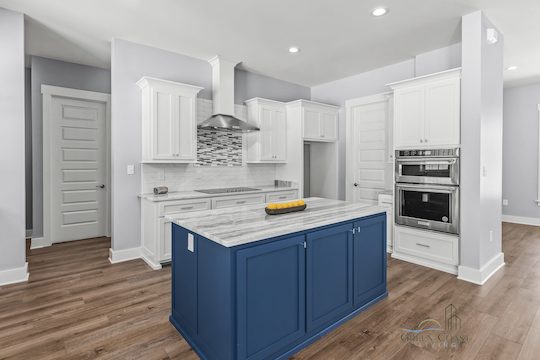 A modern designer kitchen with white cabinets, stainless steel hardware and appliances, and granite countertops. A bold yet classy navy blue island stand proudly in the middle.